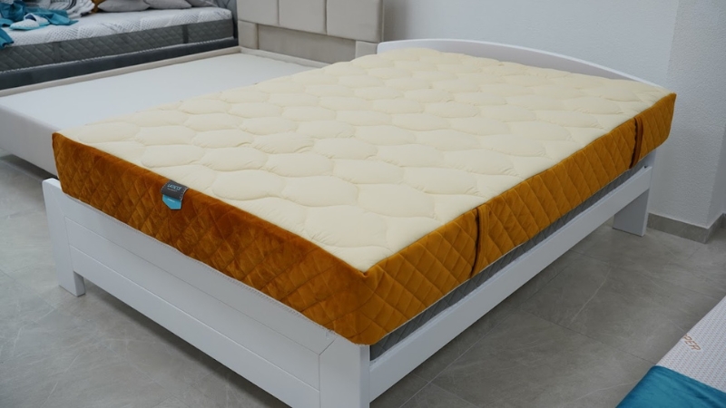 Dušek svetložute boje sa prošivenom navlakom, postavljen na beli drveni krevet u moderno uređenoj spavaćoj sobi