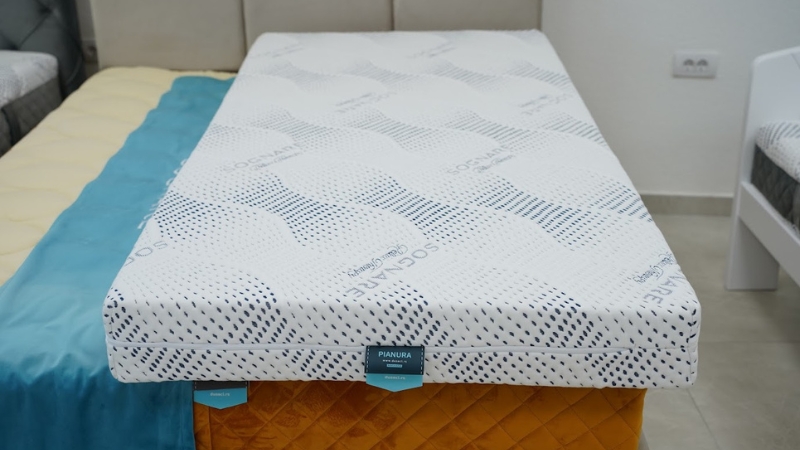 Moderan dušek sa oznakom „Pianura“ postavljen na postelju sa senfnožutim prekrivačem i tirkiznim prekrivačem sa strane