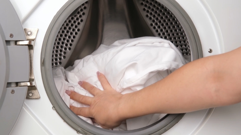 Osoba stavlja belu posteljinu u veš mašinu radi pranja na 60°C