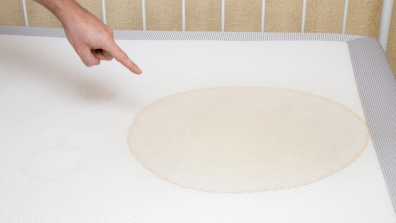 Čovek prstom pokazuje fleku od mokraće na dušeku