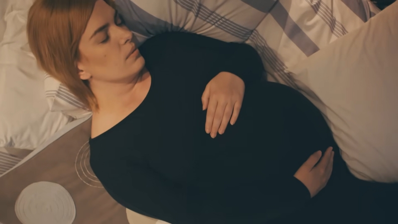 Trudnica spava u krevetu na leđima sa rukama na stomaku